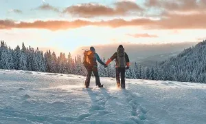 koppel wandelt door de sneeuw in een bebost, bergachtig landschap