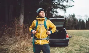 man met gele jas en rugzak staat voor een auto met open koffer