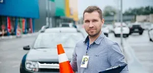 VAB-rijlesgever staat voor een auto met een clipboard en oranje kegeltje in de hand