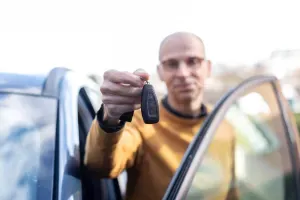 een man staat achter een open portier van een auto en houdt een autosleutel omhoog