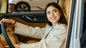 vrouw met beige jas zit achter het stuur van een auto