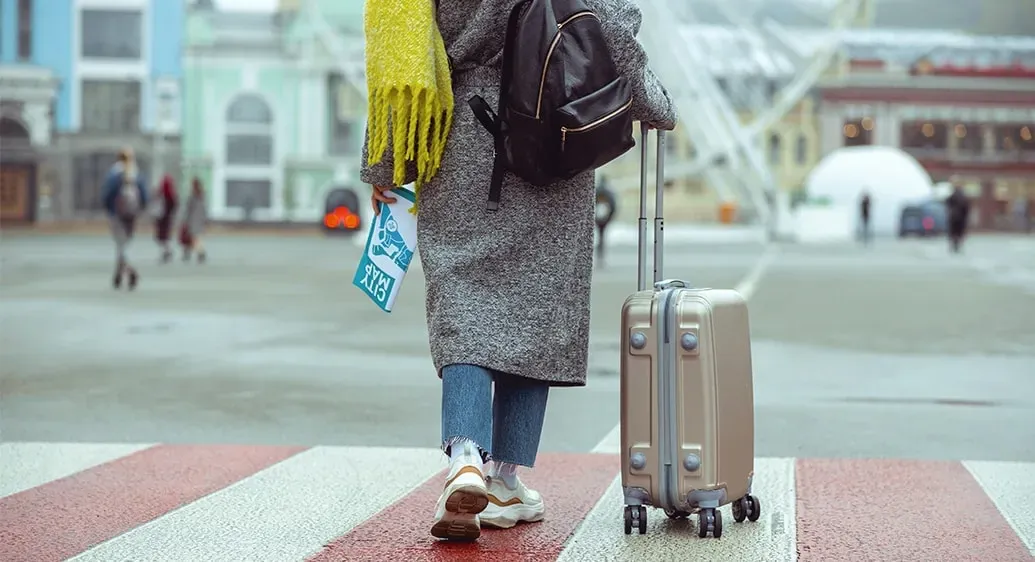 vrouw met winterse kleren en handbagagekoffer loopt rond in stad
