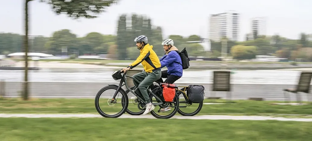 twee mensen op elektrische fietsen rijden snel voorbij een stad die wazig te zien is op de achtergrond
