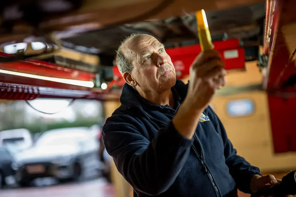 autotechnieker inspecteert de onderkant van een auto met een zaklamp