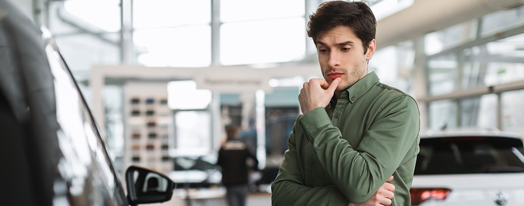 een man kijkt nadenkend naar een auto in een showroom