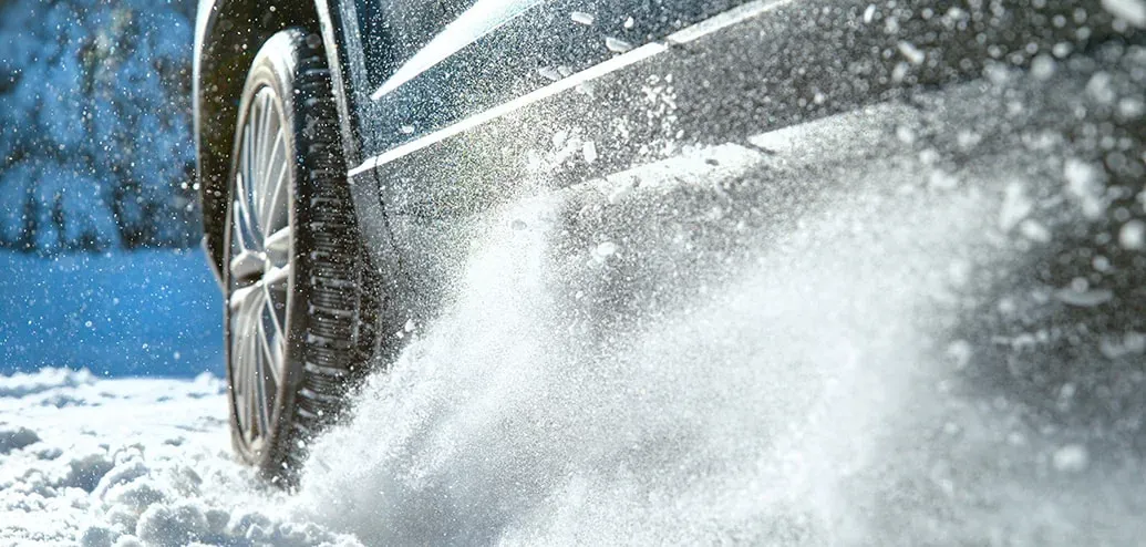 actiefoto van een auto die over sneeuw rijdt en sneeuw doet opvliegen