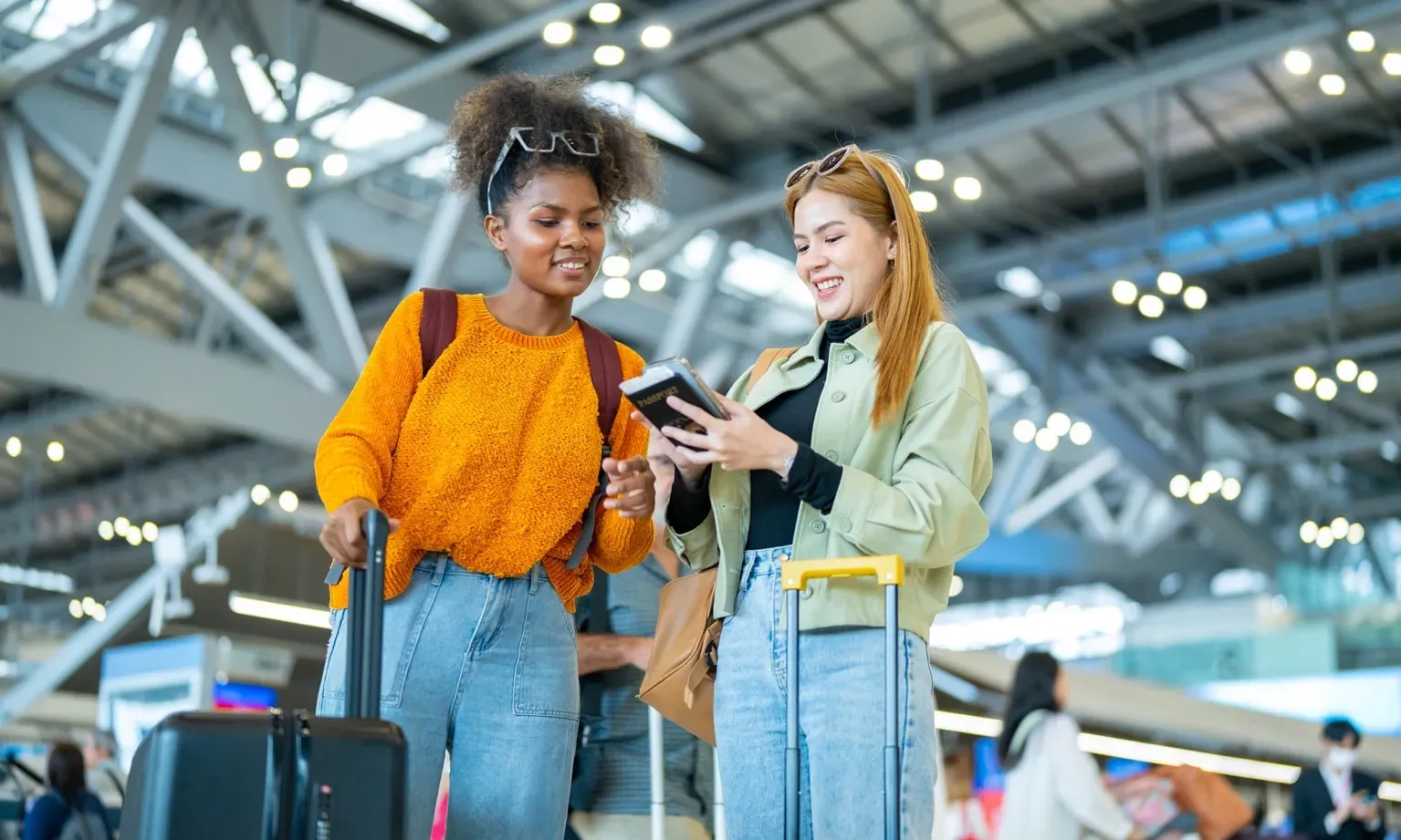 Twee reizigers bekijken samen een smartphone in een moderne luchthaven met bagage.